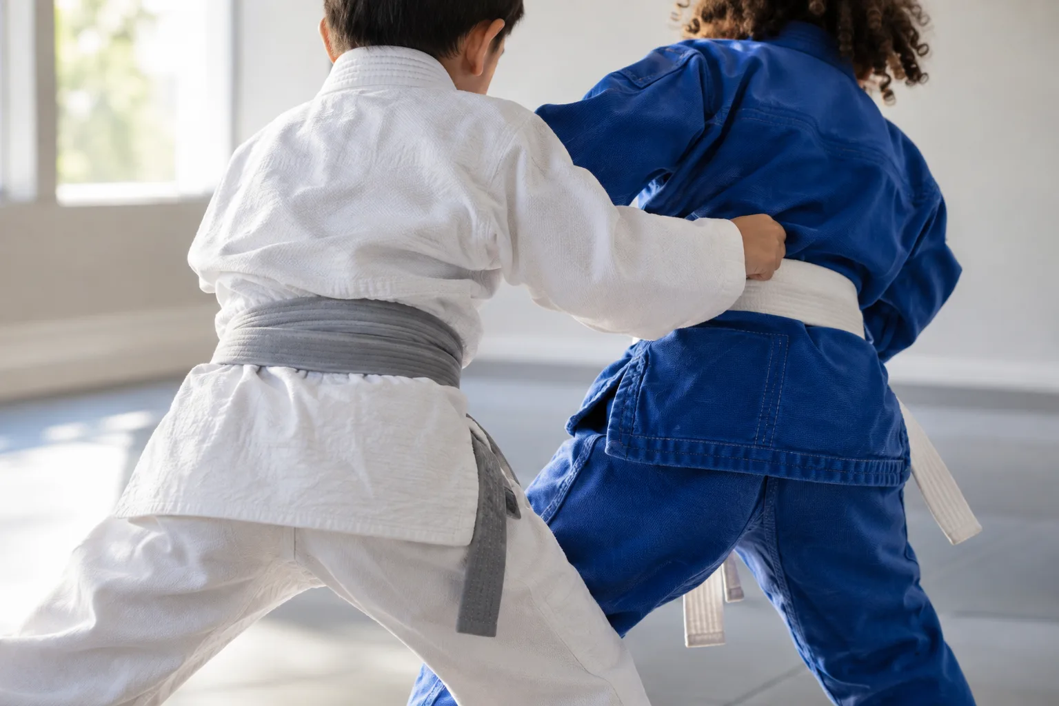 Children practicing karate, taekwondo, and jiu-jitsu techniques together in a bright martial arts studio.