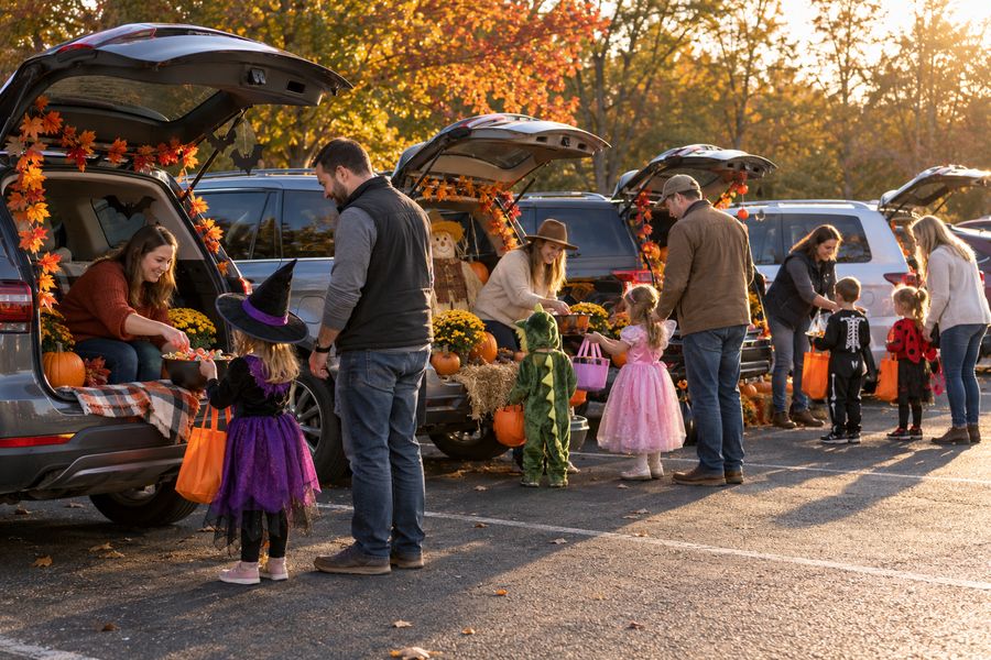 Families trunk-or-treating at a row of decorated cars.